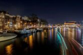 Amsterdam canal at night with lit canal houses and moored boats reflected in the water