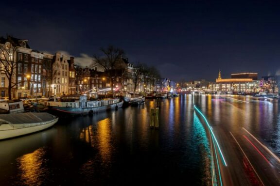 Amsterdam canal at night with lit canal houses and moored boats reflected in the water