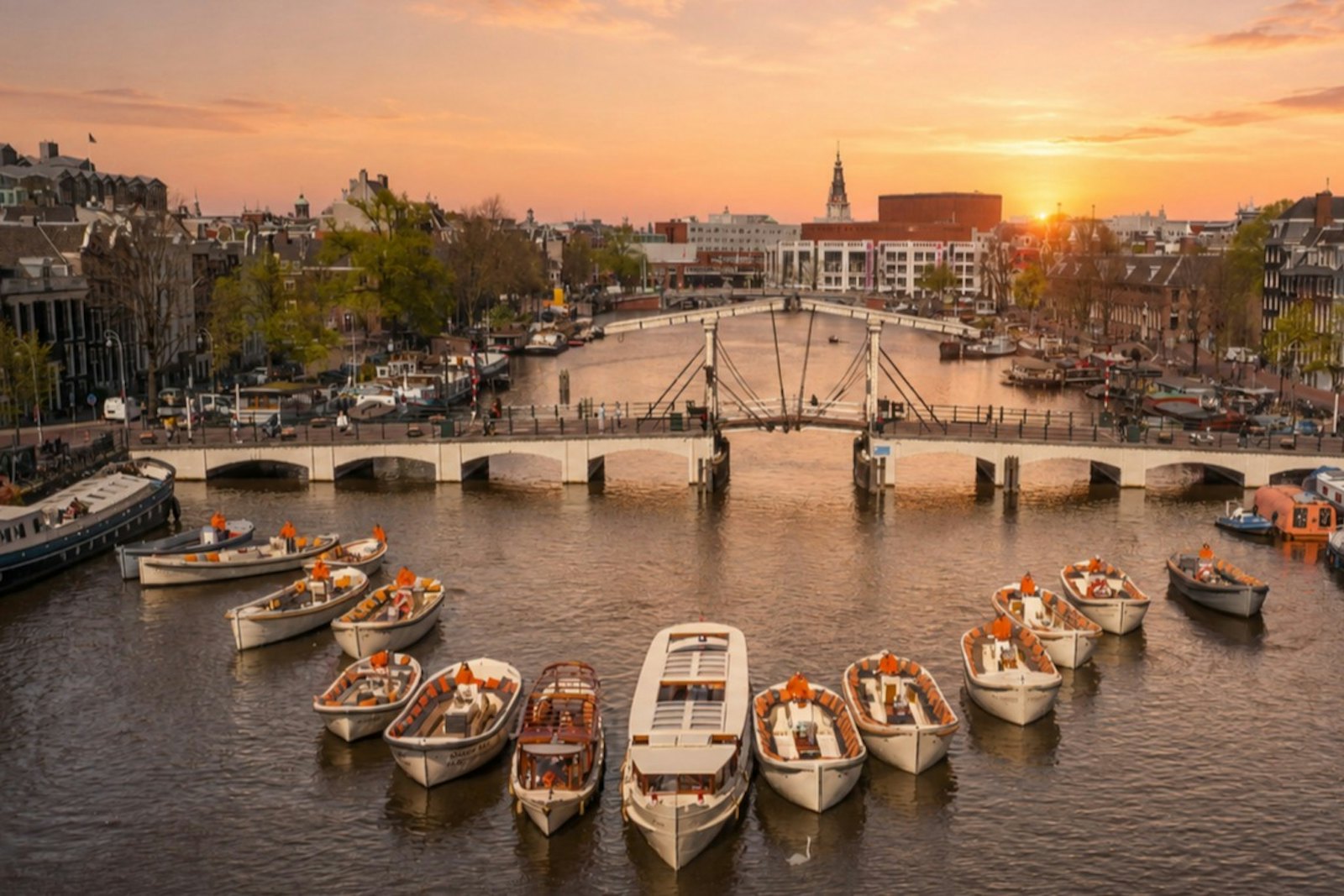 Open canal boats moored near the Magere Brug on the Amstel at sunset