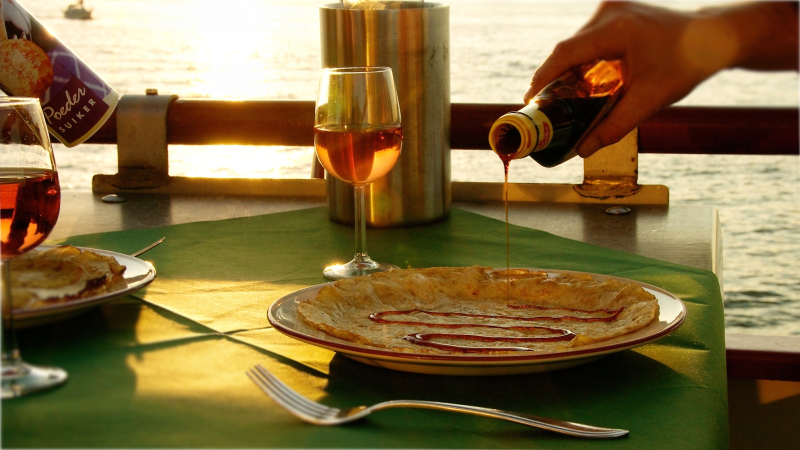 A Dutch pancake with syrup being poured over it at a window table on board
