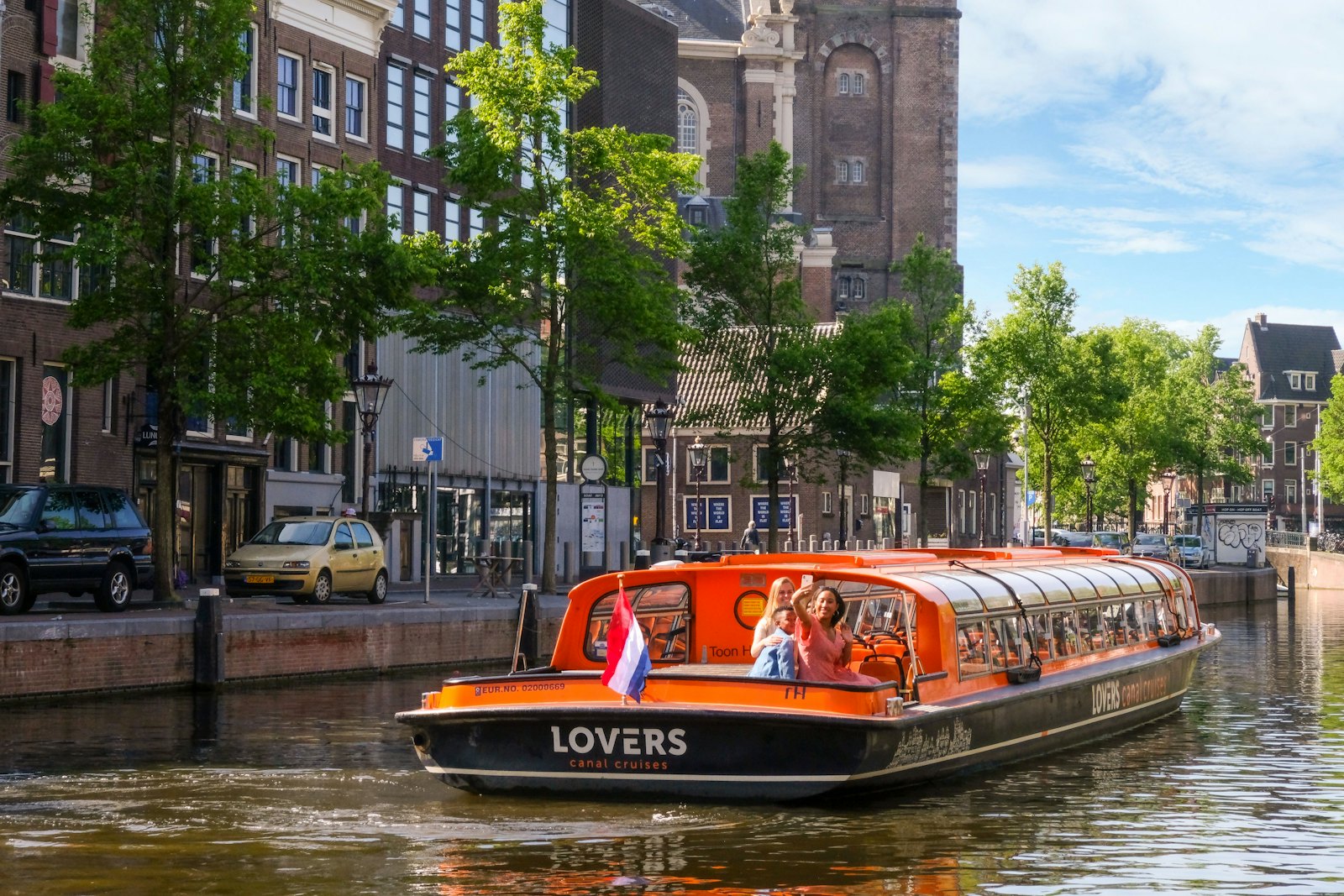 Passengers boarding an orange canal cruise boat on the Prinsengracht near the Westerkerk