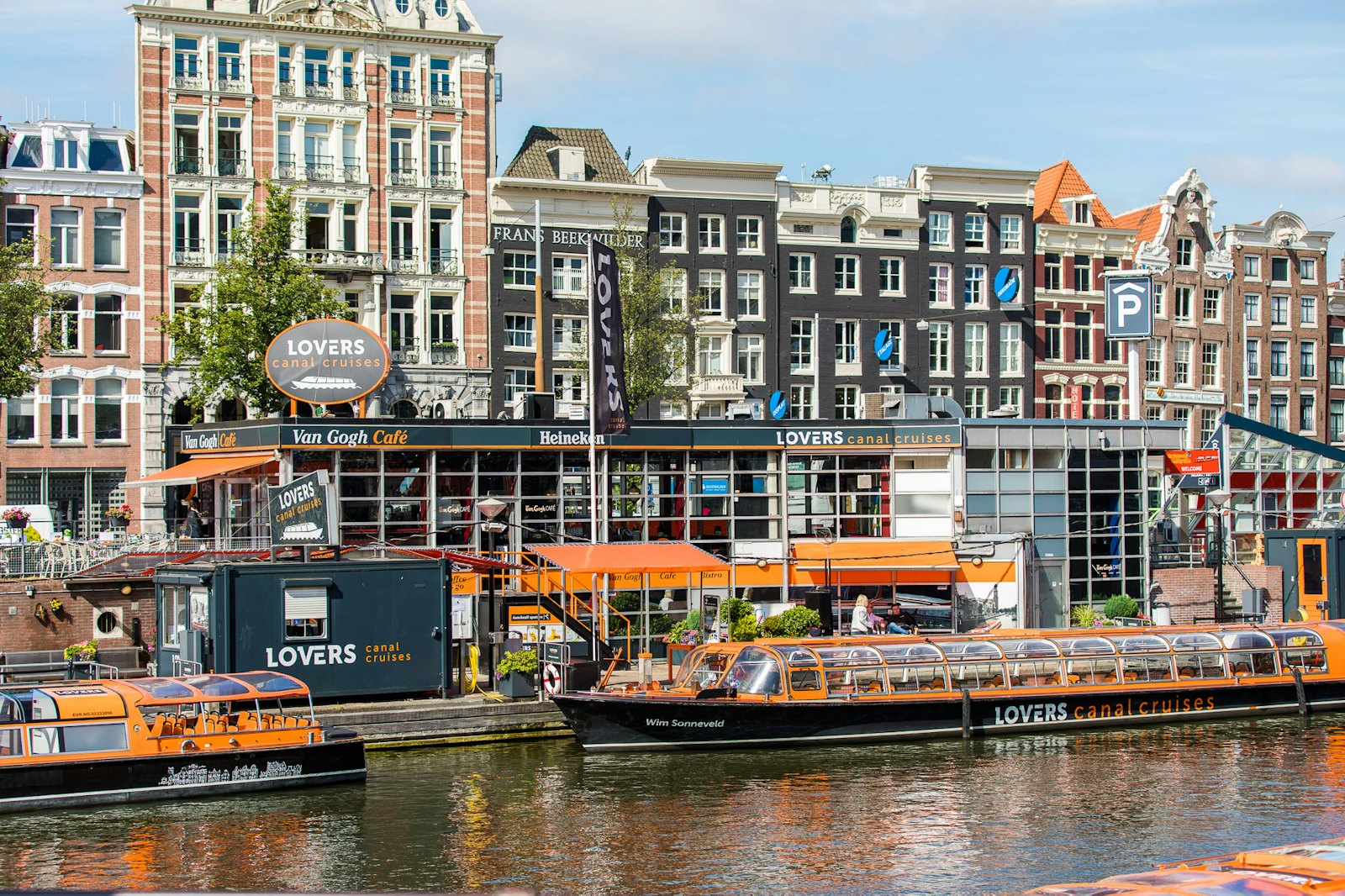 Several orange canal cruise boats moored at their pier along an Amsterdam canal